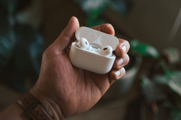 Close-up of a person holding an open case of Apple AirPods Pro 2, with a blurred background of indoor plants