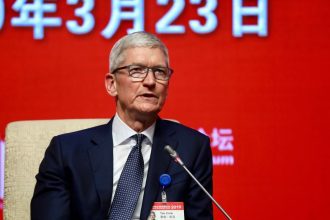 Apple CEO Tim Cook speaking at a conference in China on March 23, 2019, with a red background displaying the date in Chinese characters