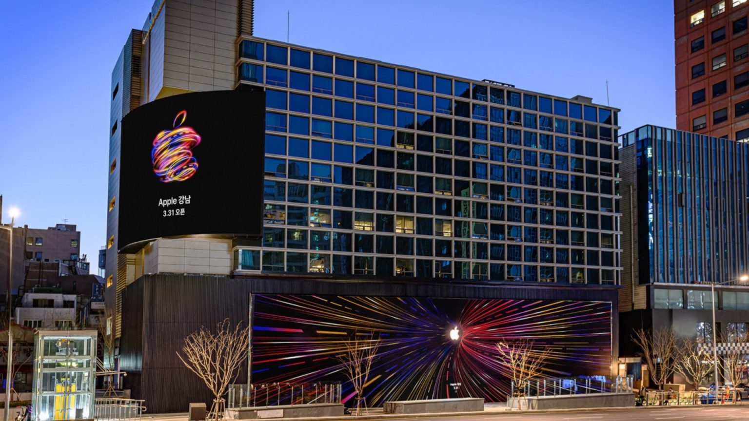 Exterior of the new Apple Store in Gangnam, South Korea, featuring colorful neon Apple logo displays and a large opening announcement billboard on the building facade