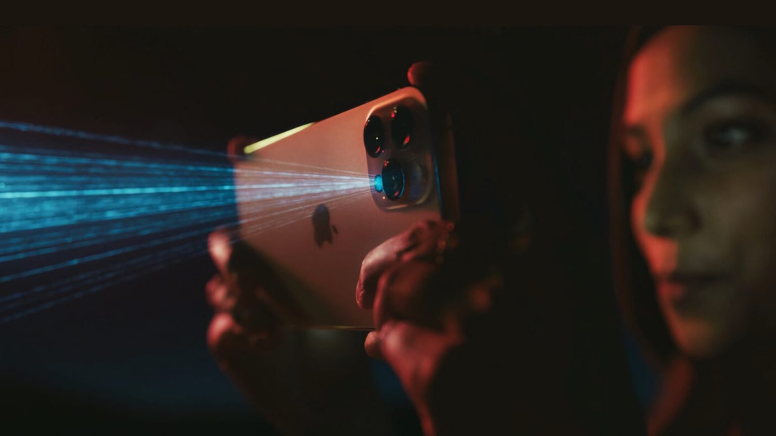 Close-up of a woman holding an Apple iPhone with a LiDAR sensor, showing blue laser beams added in post-production, in a dimly lit environment