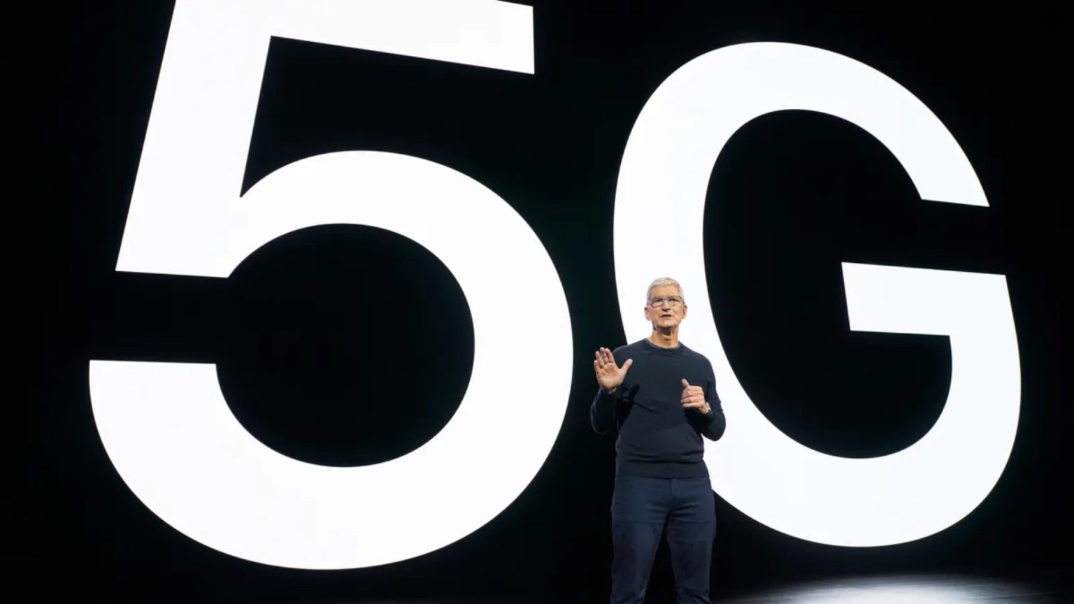 Apple CEO Tim Cook presenting in front of a large ‘5G’ backdrop, emphasizing the company’s commitment to 5G technology