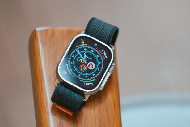 The image shows an Apple Watch Ultra resting on a wooden surface. The watch has a rugged design with a silver titanium case and a black sport loop band. The watch face is illuminated, displaying various metrics such as activity rings, date, air quality index (AQI), and a contact photo