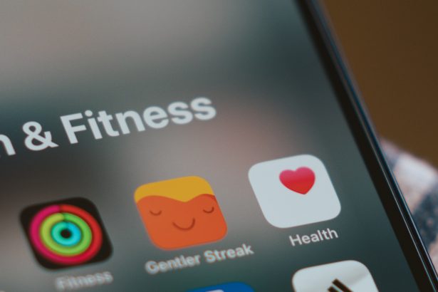 The image shows a close-up of an iPhone screen displaying a folder titled “Health & Fitness.” Within the folder are various app icons, including Apple’s Fitness app with colorful activity rings, the Gentler Streak app with a relaxed face icon, and Apple’s Health app with a pink heart on a white background. The screen is slightly blurred around the edges, focusing on the app icons.