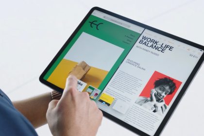 A person interacts with an Apple iPad running iPadOS. The screen displays a split-view with two apps side-by-side. On the left, a website with a green and yellow theme shows an image of a paper bag and some text. On the right, a digital magazine or article titled “WORK-LIFE BALANCE” features a black and white photo of a smiling person with a red background. The person’s hand is tapping on the screen, demonstrating the device’s multitasking capabilities.