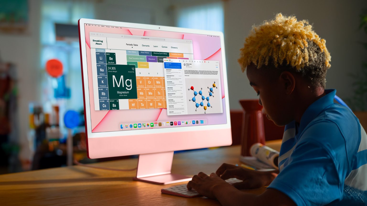 A student working on a pink Apple iMac, displaying a periodic table and molecular structure, in a brightly lit room