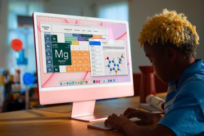 A student working on a pink Apple iMac, displaying a periodic table and molecular structure, in a brightly lit room