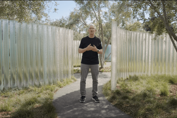 Apple CEO Tim Cook standing outdoors among tall glass pillars and trees, delivering a presentation in a tranquil garden setting